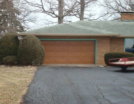 Garage of a brick house with brown door; a trailer is parked in the driveway.