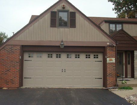 Tan garage door with decorative black hardware, tan and brick exterior, brown trim.
