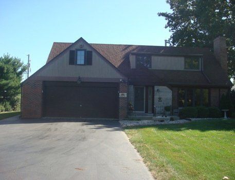 Two-story house with dark garage door, brick and siding, and green lawn.