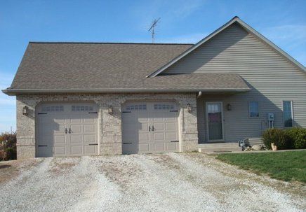 Three-car garage with gray doors and gravel driveway; house with tan siding and a clear blue sky.