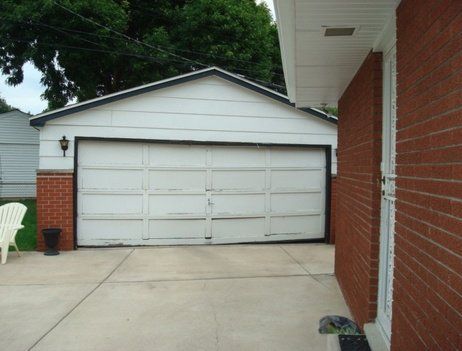 White garage with a closed door, red brick wall, and concrete driveway.