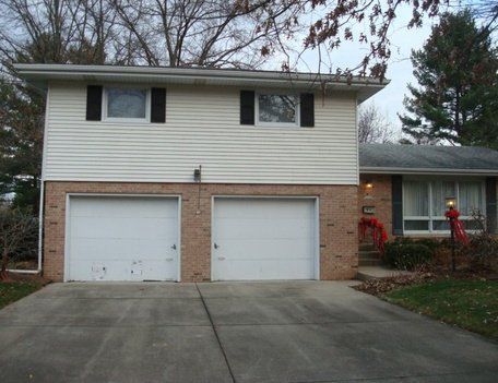 Two-story white house with a brick base and two garage doors. A driveway leads up to the house.