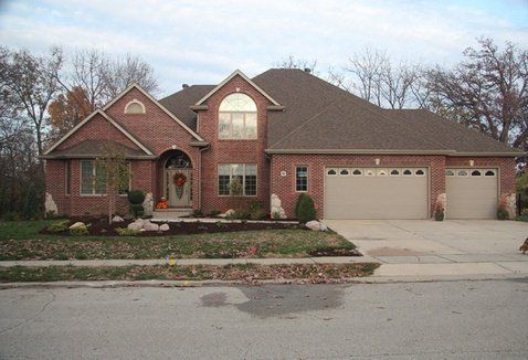 Brick house with three-car garage, arched doorway, and manicured lawn.