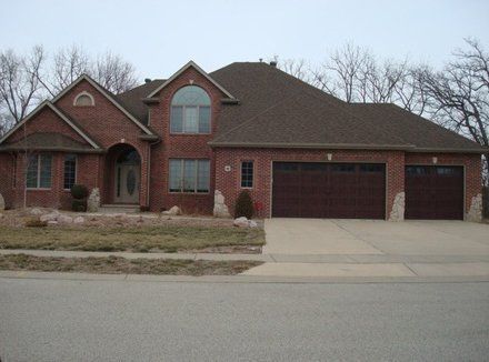 Brick house with brown roof, three-car garage, and bare trees in the background.