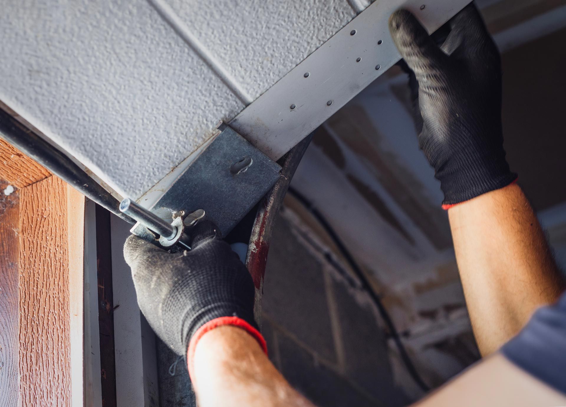 Gloved hands adjusting a metal bracket on a garage door track.