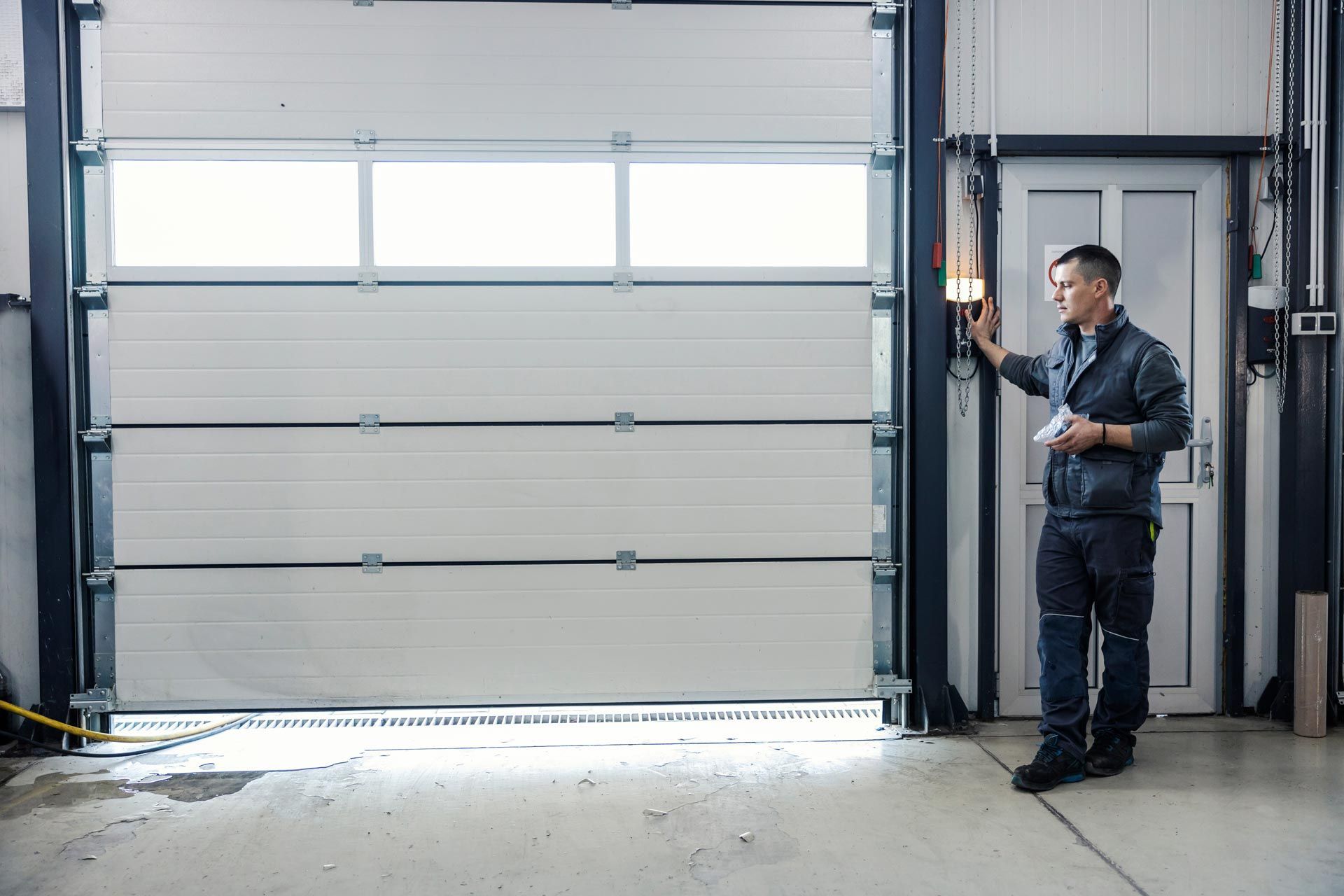 Worker standing by a large gray industrial garage door in a warehouse.