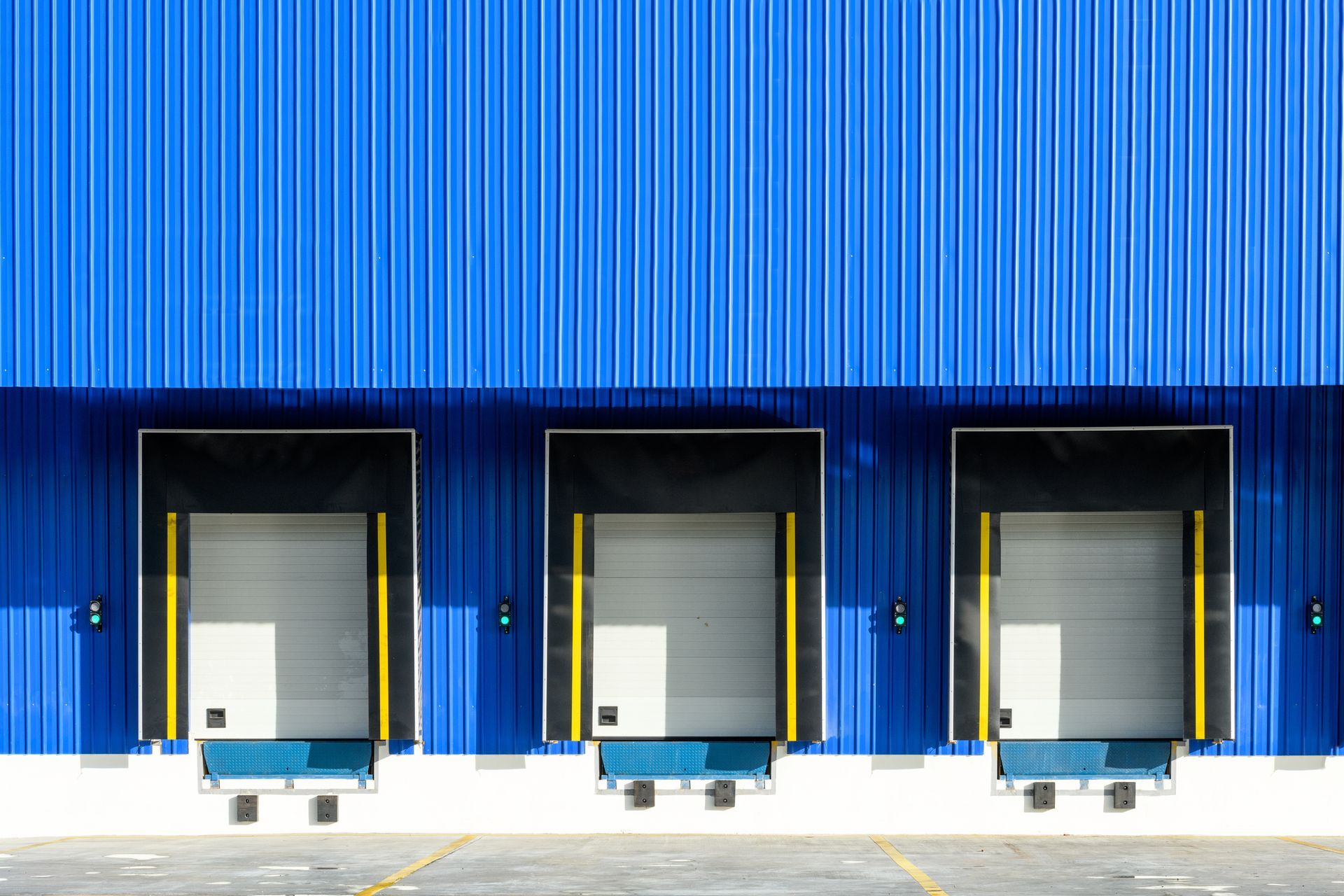 Three loading docks with closed doors against a blue industrial building.