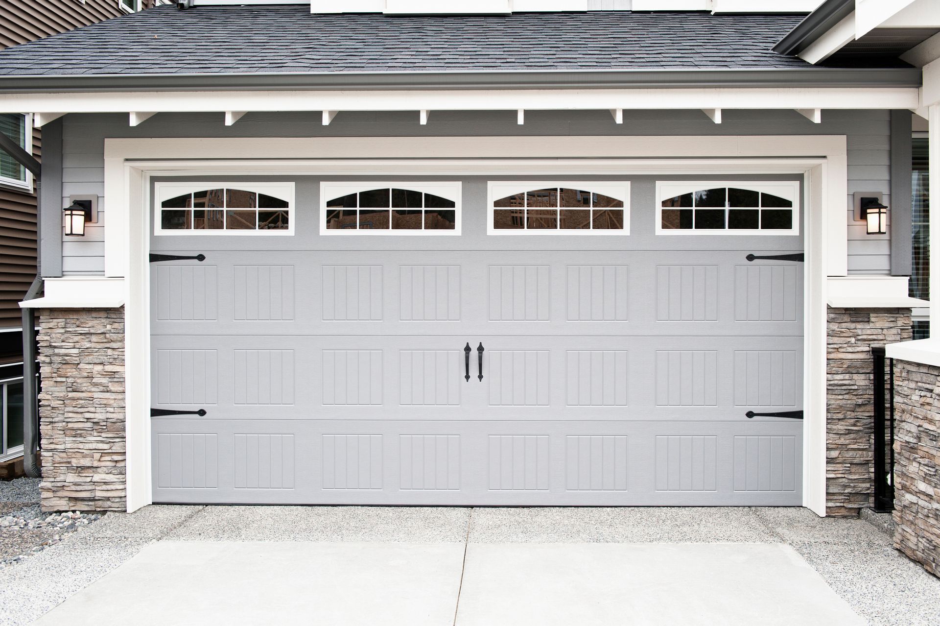 Gray garage door with windows, stone accents, and black hardware.