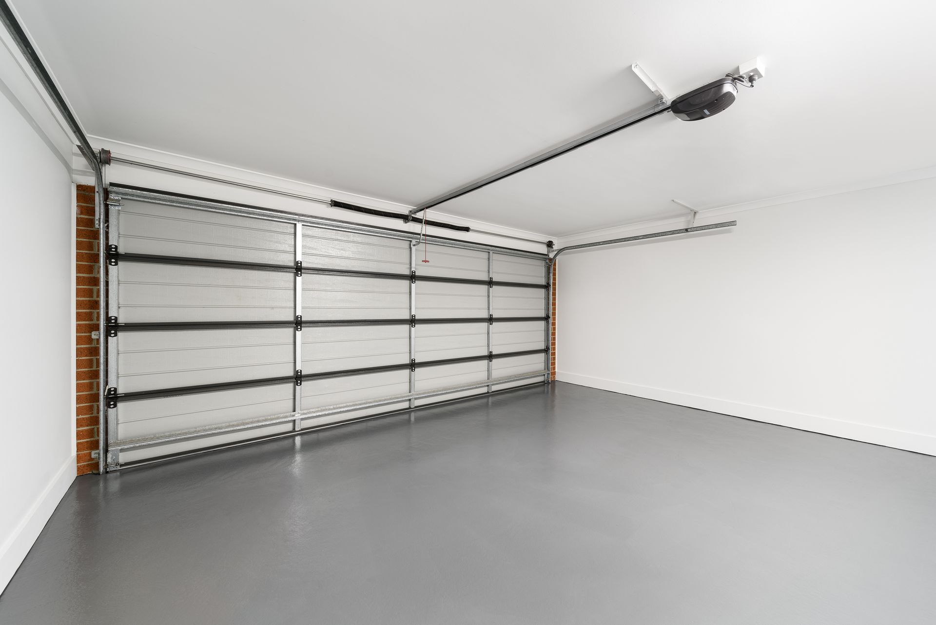 Empty garage with gray floor, white walls, and closed silver door.