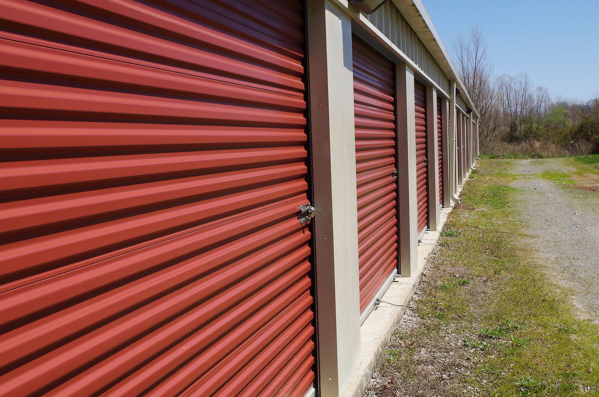 Row of red storage unit doors in a building with beige trim, set along a gravel path.