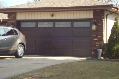 Brown garage door with rectangular glass windows, brown car parked on driveway.