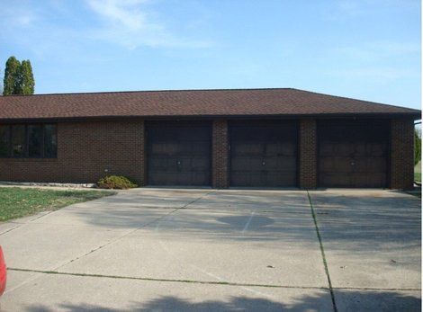 Brick building with three garage doors and a concrete driveway under a blue sky.