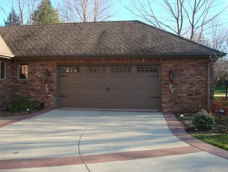Brick house with tan garage door, driveway, and brick border.