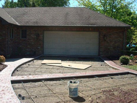 Driveway under construction with rebar grid, framed by concrete walkways, in front of a brick garage.