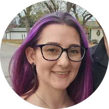 Woman with purple hair and glasses smiling outdoors.