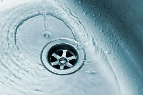 Water flowing into a drain in a stainless steel sink.
