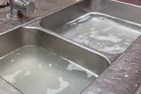 Two-basin stainless steel kitchen sink filled with cloudy water and soap suds.