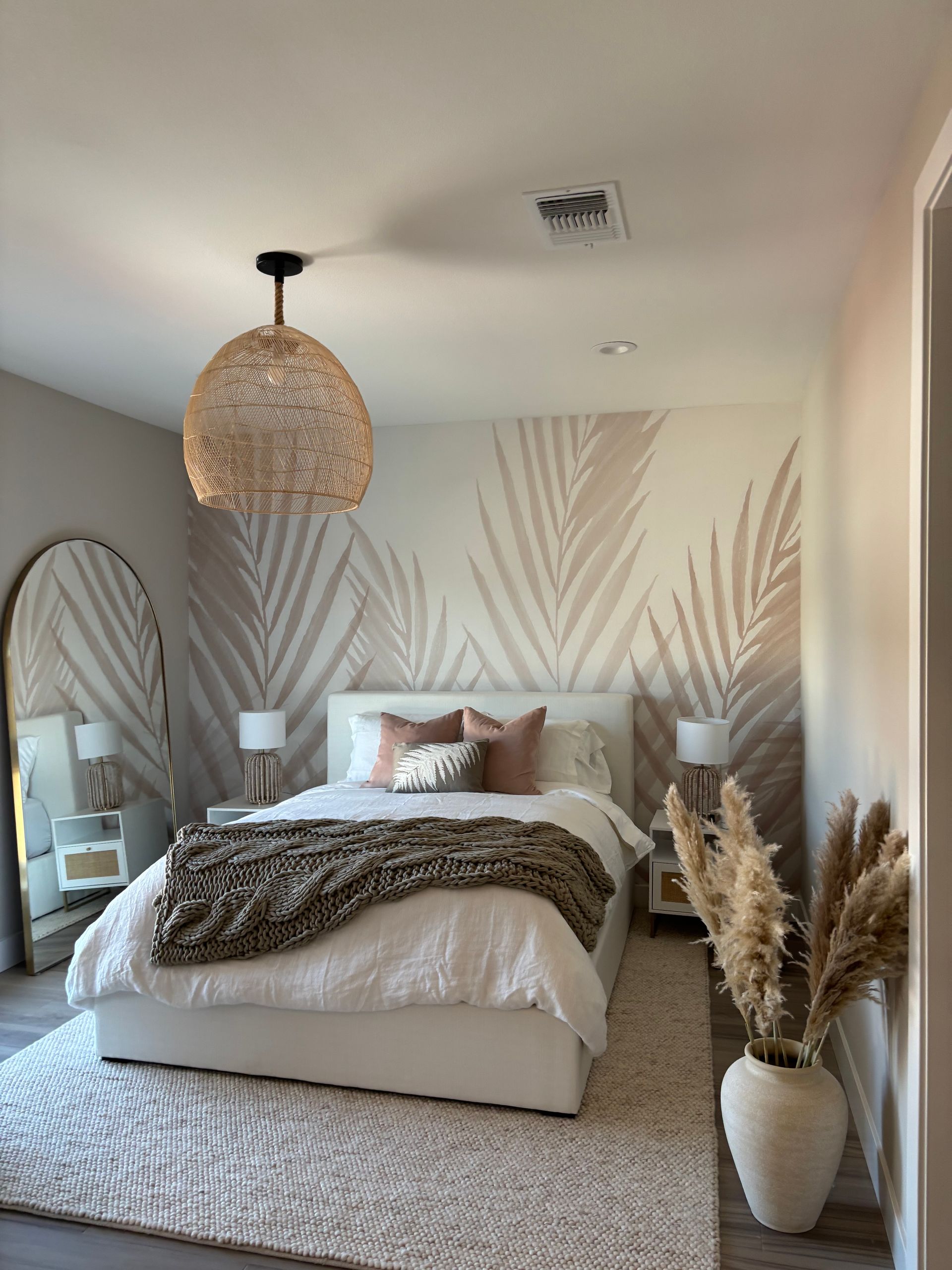 A bedroom with a large bed , a large mirror , and a wall with palm leaves painted on it.