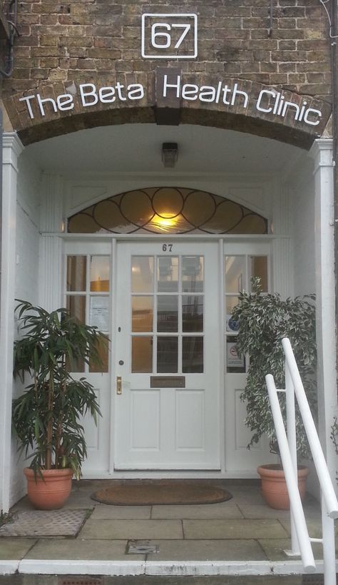 The entrance to our building with stone porch and white front door flanked by plants in tubs