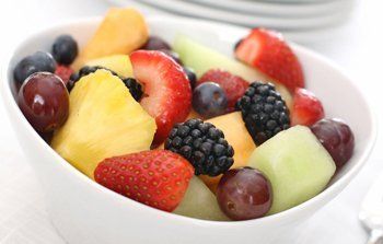 A white bowl of fresh melon, berries and grapes