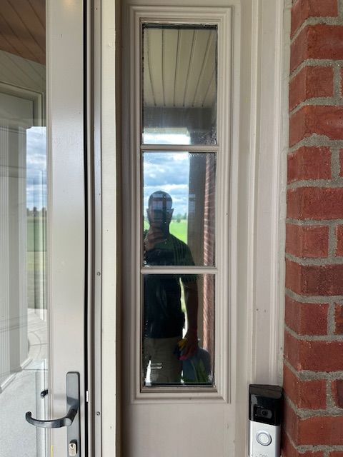 Person reflected in window of white door, brick exterior with Ring doorbell.