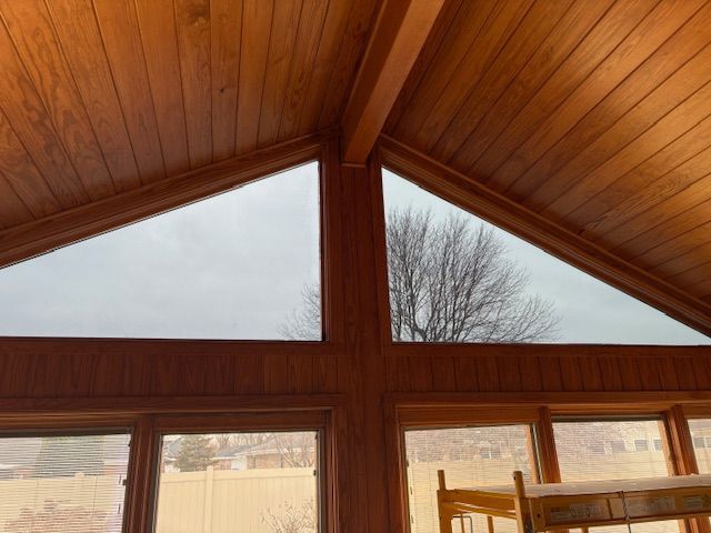 Wooden paneled room with triangular windows showing an overcast sky and a bare tree.