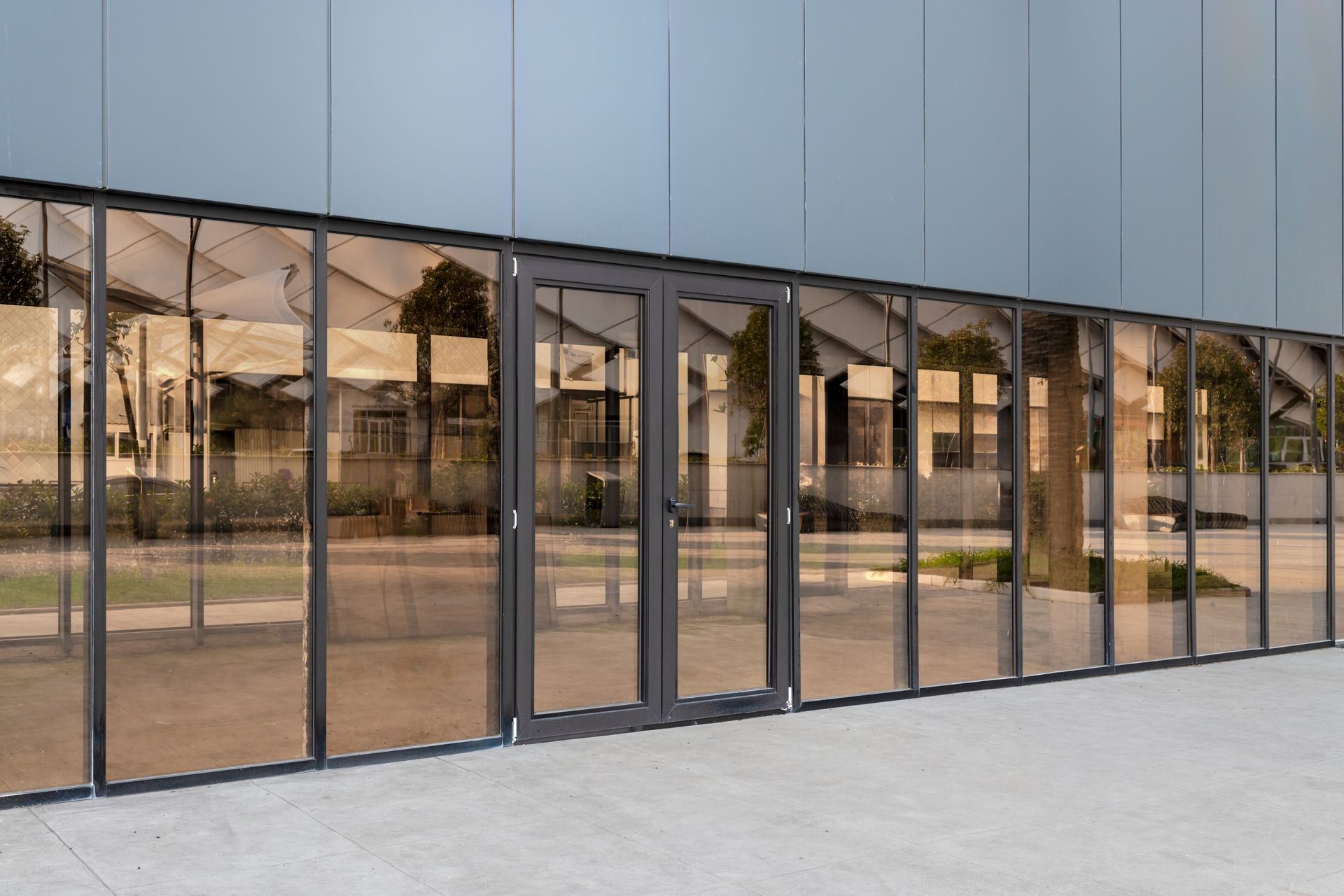 Exterior view of building with glass panels and double doors, gray frames, concrete surface.