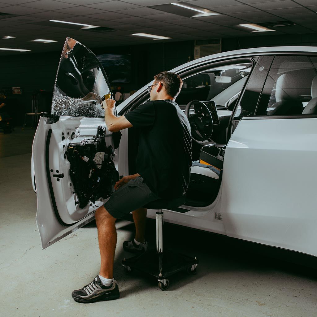 Man installing car door panel, seated, in a shop.