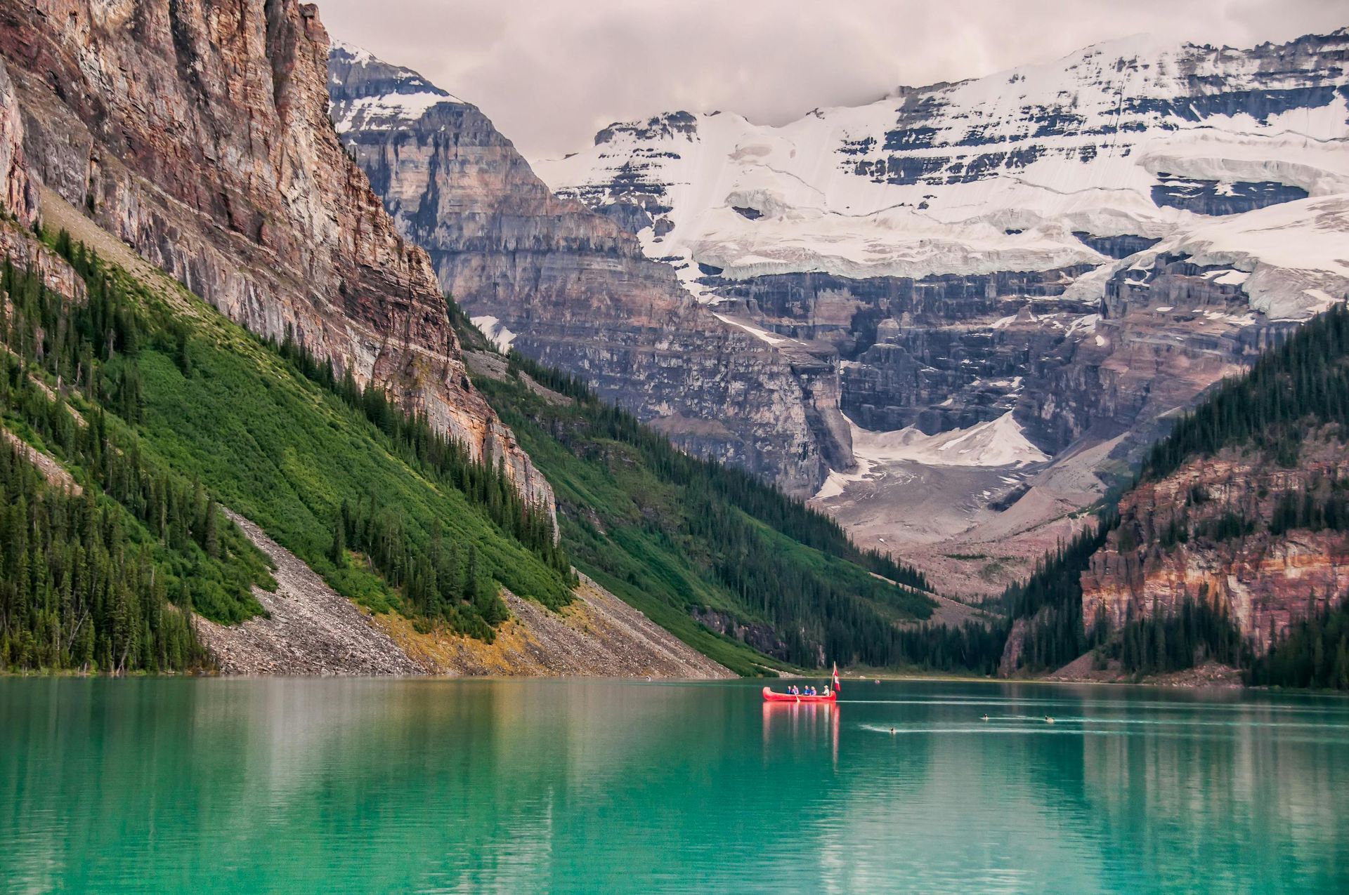 Turquoise lake with a red canoe, surrounded by mountains and snowy peaks.