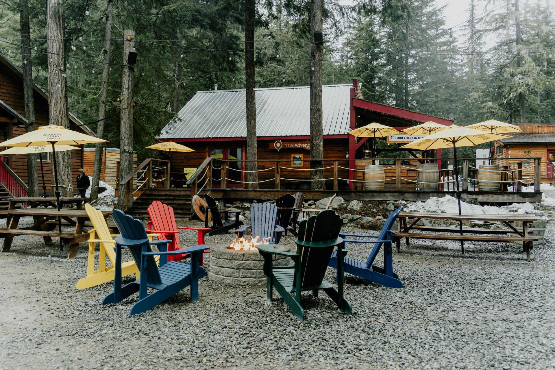 A colorful outdoor seating area with Adirondack chairs around a fire pit, in front of a lodge-like building.