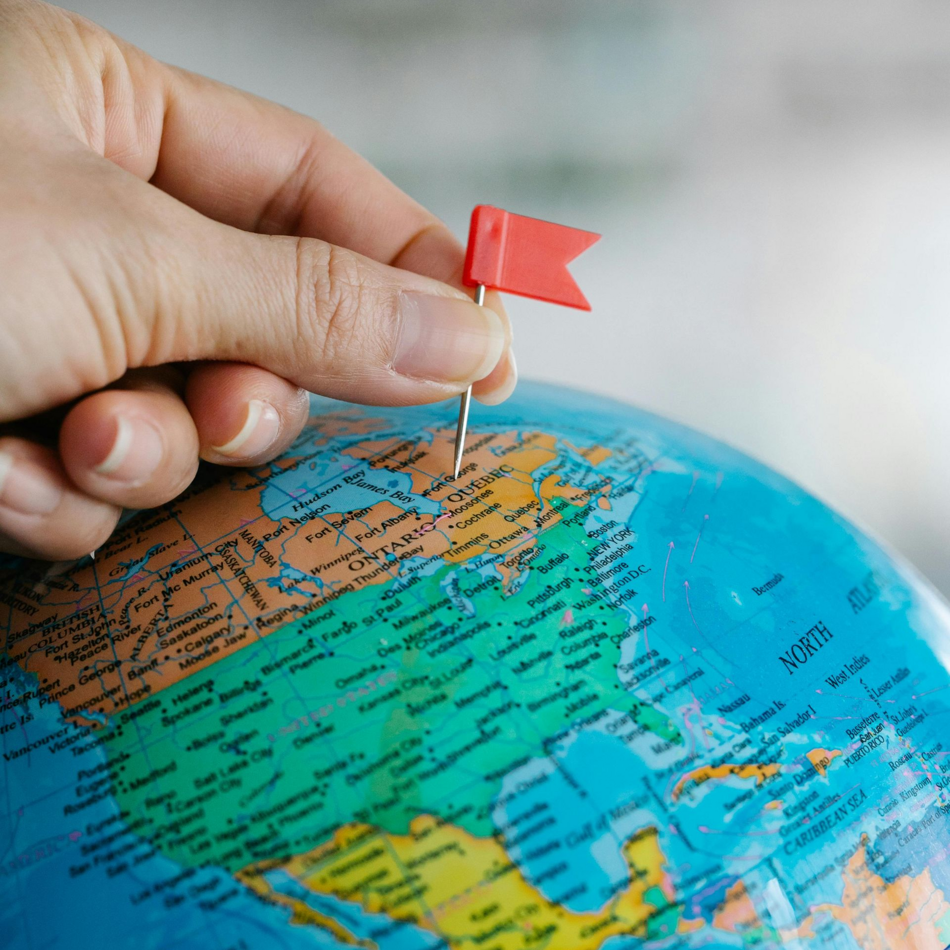 Hand placing a red flag pin on a globe, marking a location in North America.
