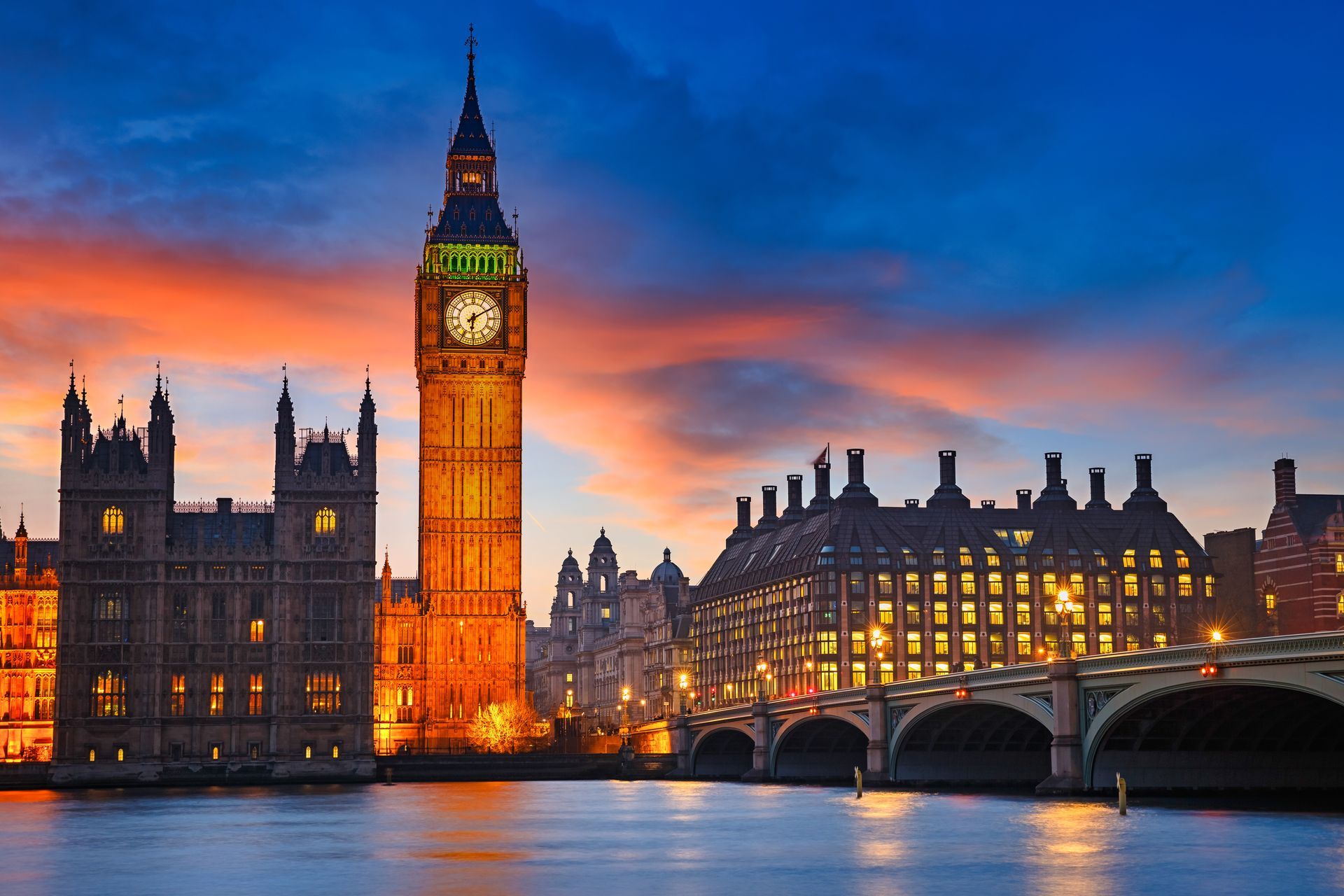 Big Ben clock tower and Westminster Palace illuminated at sunset over the River Thames, London.