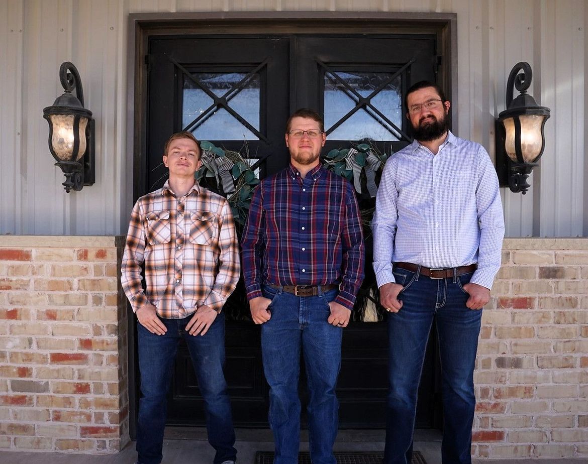 Three men are standing in front of a door.