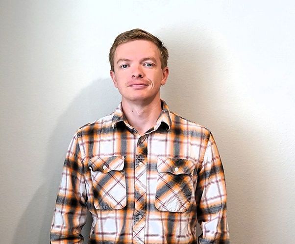 A man in a plaid shirt is standing in front of a white wall.