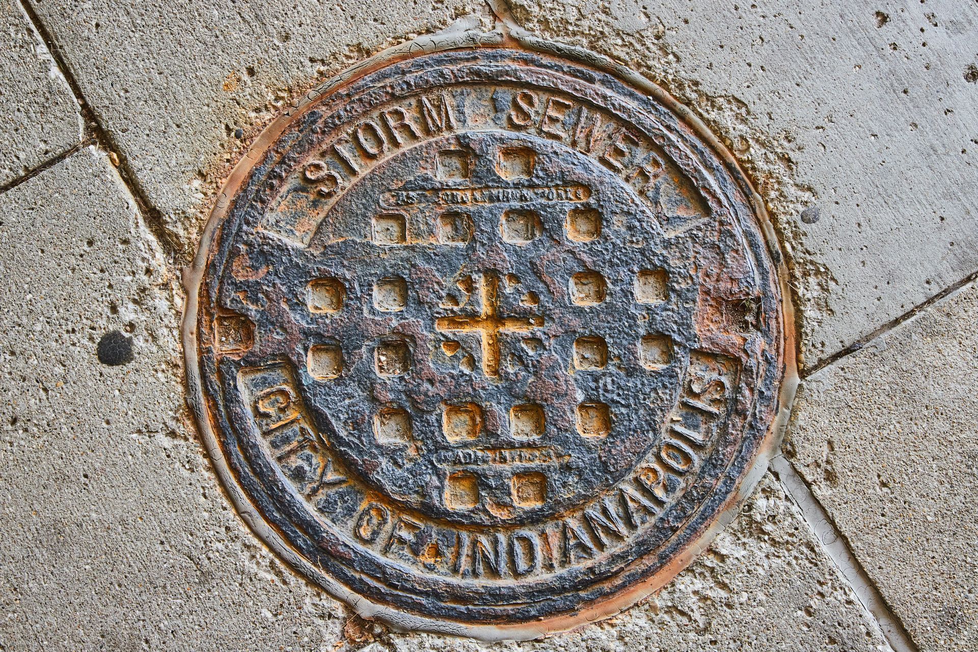 A manhole cover for the city of indianapolis is on the sidewalk.