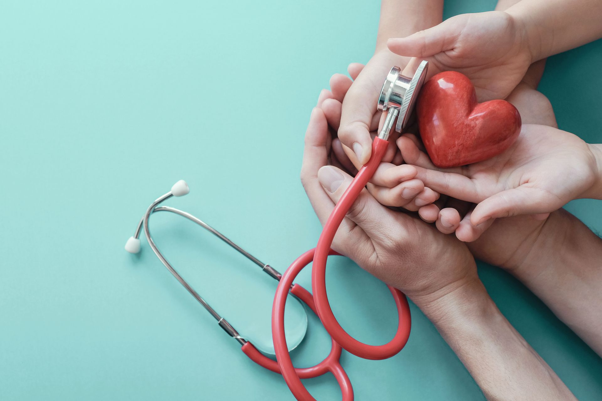 Multiple hands holding a red heart and stethoscope on a teal background.