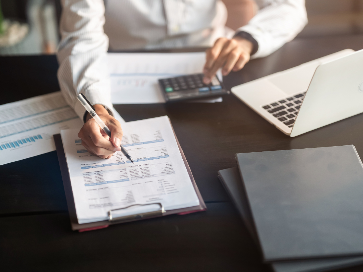 Person using a calculator, looking at documents, and working on a laptop at a desk.