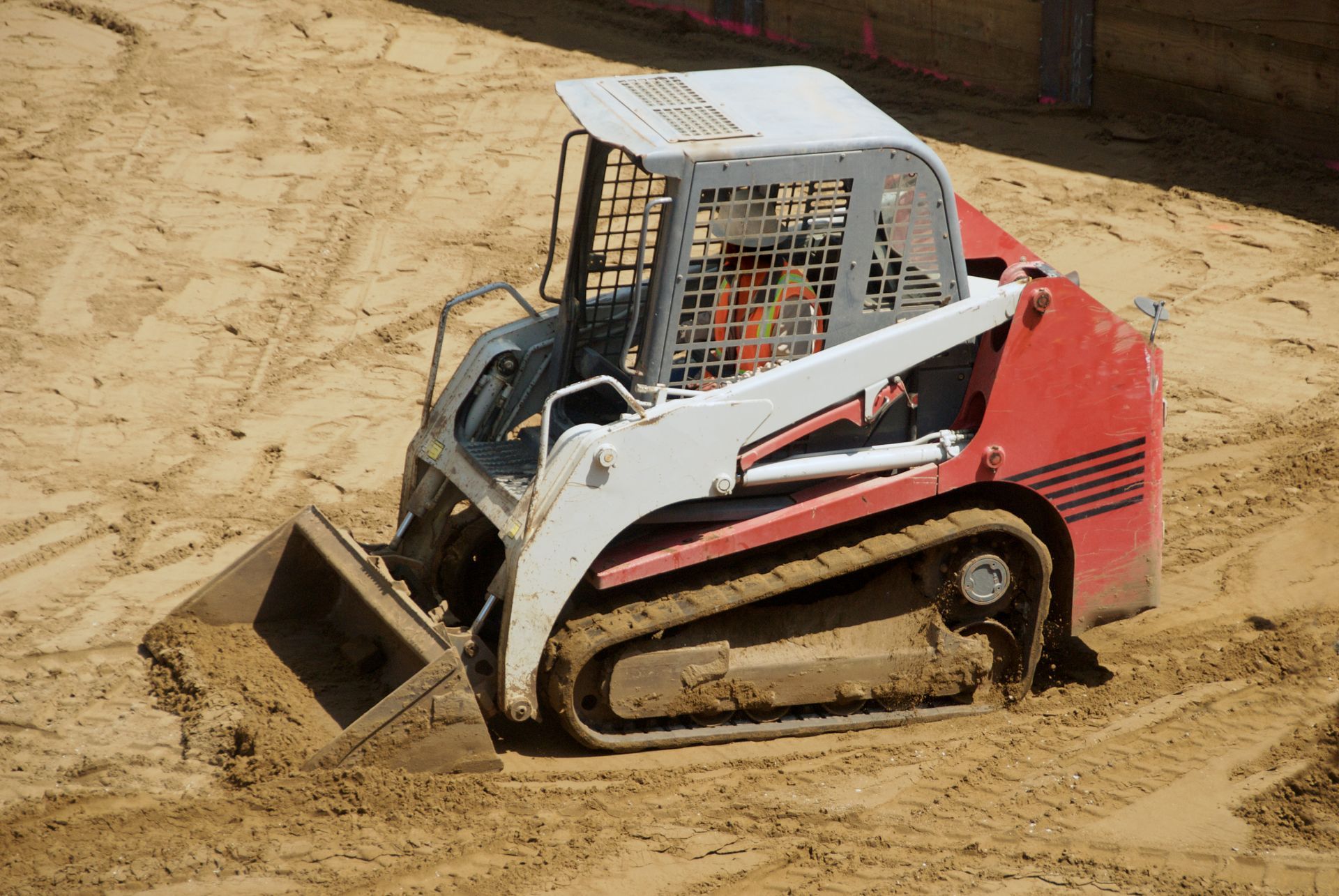 Red and white skid steer loader on a sandy construction site.