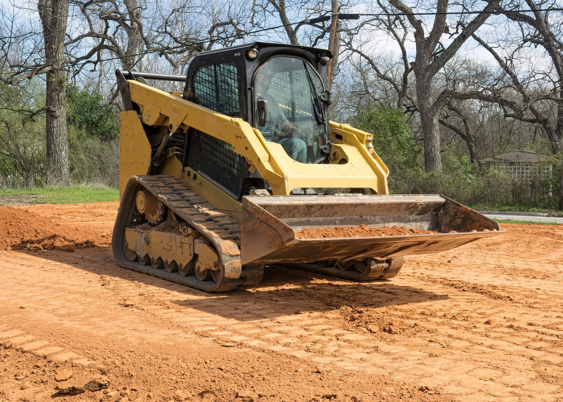 Yellow tracked skid-steer loader with a bucket moving dirt on a construction site.
