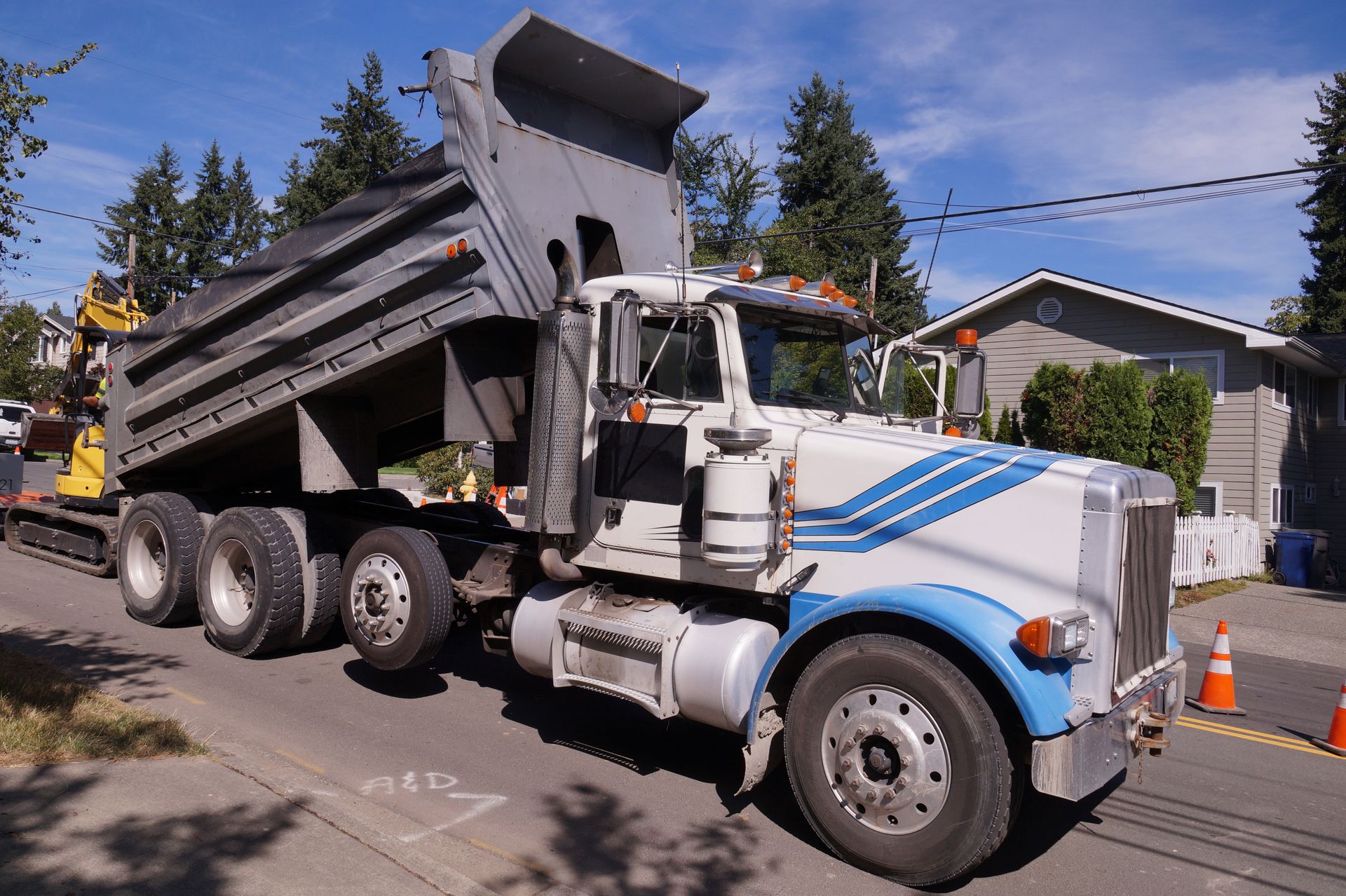 Dump truck with raised bed on a residential street. Truck is white and blue.