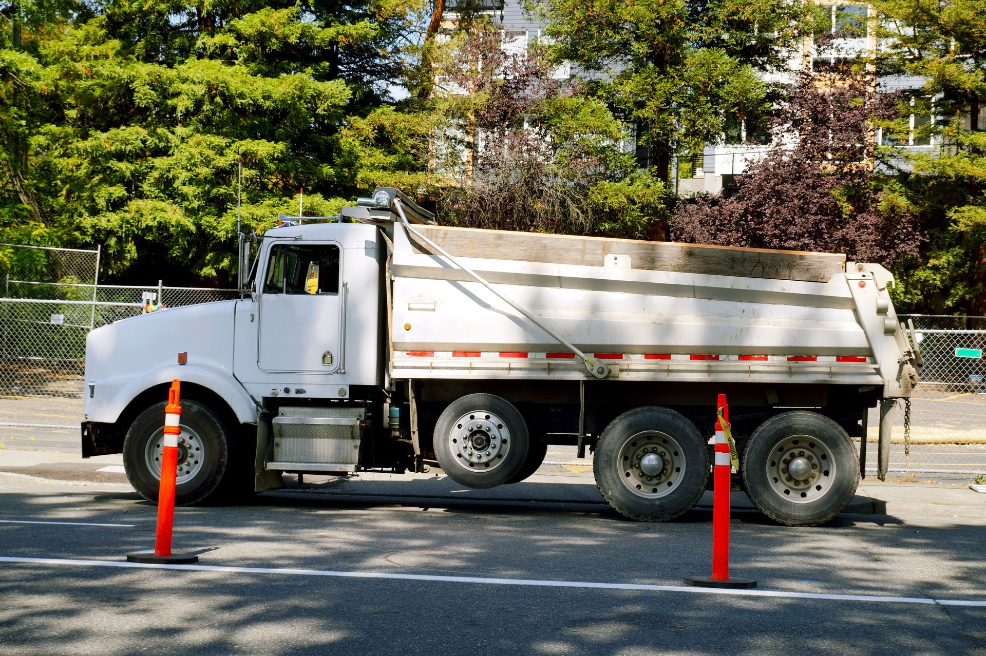 White dump truck parked on a road, with orange cones in front, trees in the background.