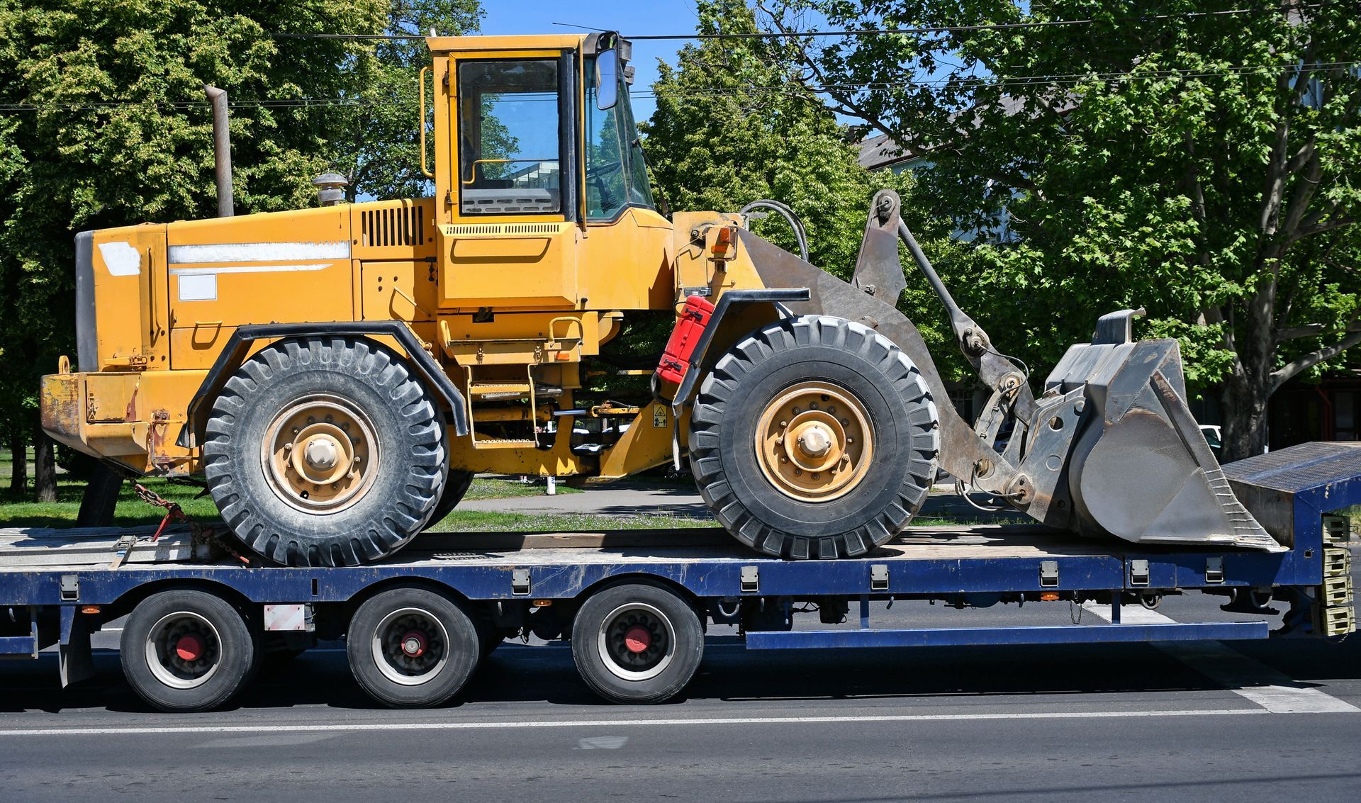 Yellow loader on a flatbed trailer, transporting heavy machinery on a road.