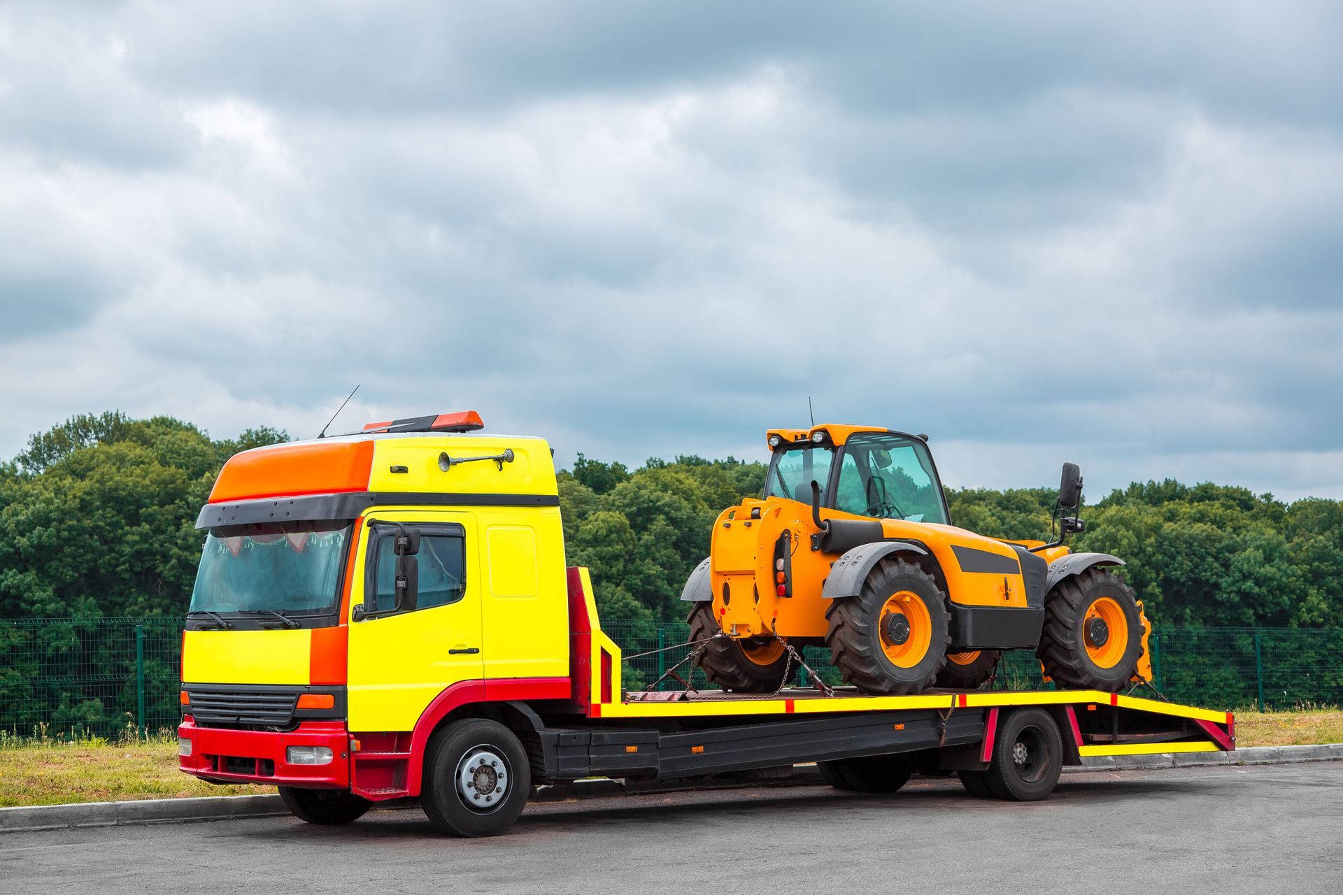 Yellow tow truck transporting an orange tractor on a cloudy day.