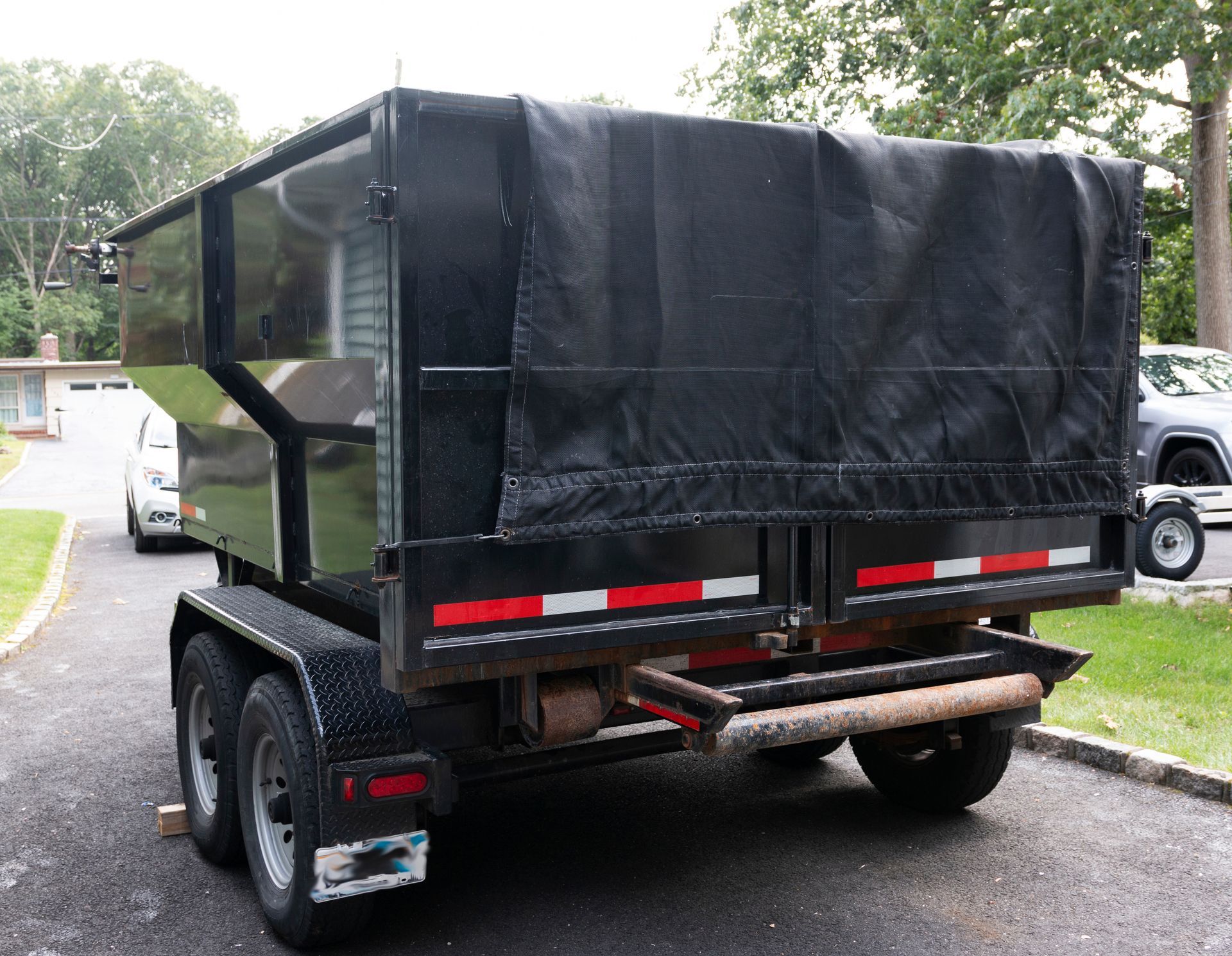 Black dump trailer with tarp cover, parked on a paved driveway.