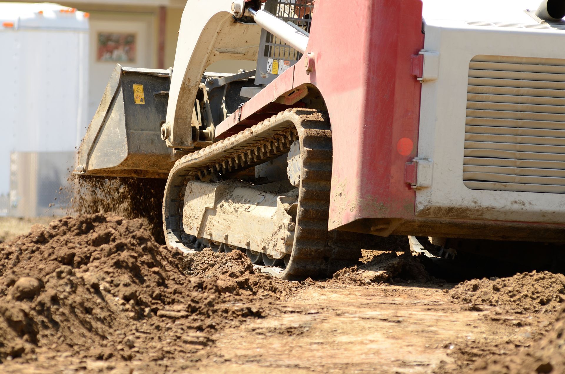 A red and white track loader scoops up dirt on a construction site.