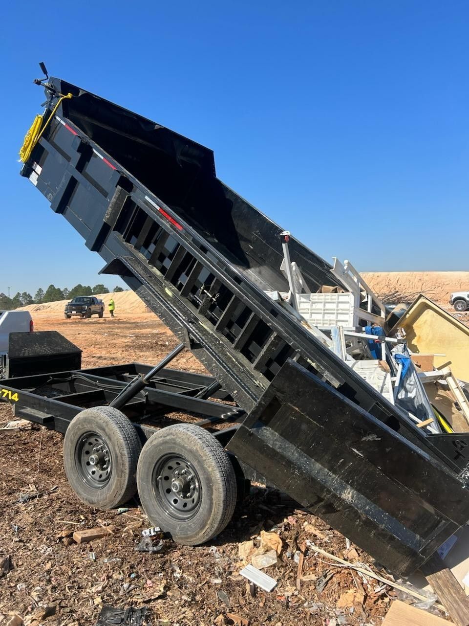 Orange skid steer with grapple lifting a tree stump on a grassy lawn.