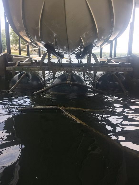 Boat on a lift, supported by inflated black buoys, in murky water.