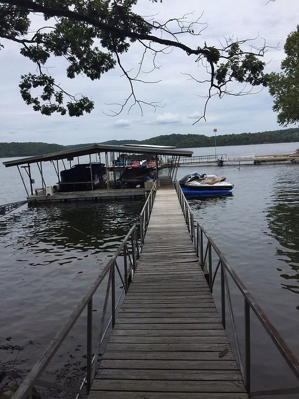 Wooden dock with railings leading to a boat dock on a lake, cloudy day.