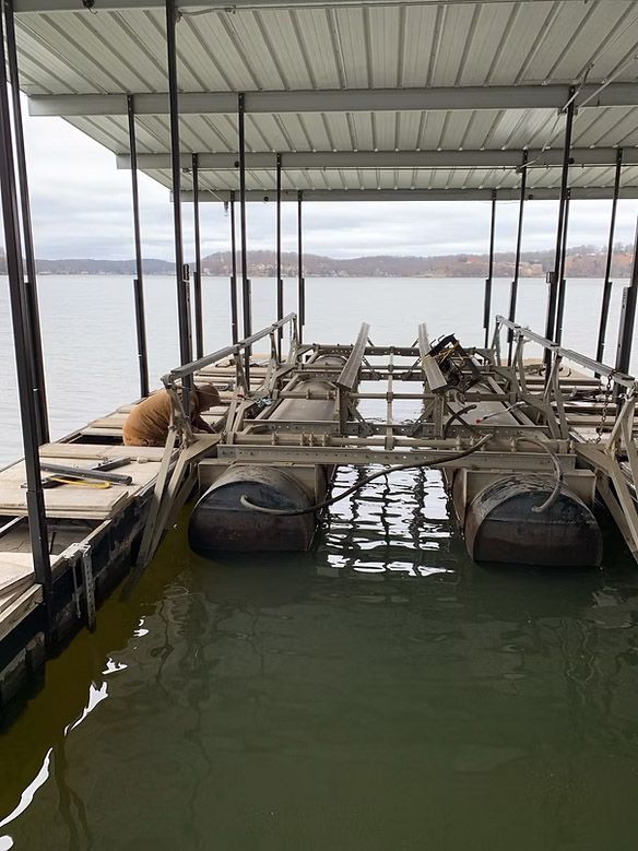 Boat dock with metal frame, pontoon floats, and a covered roof on a lake.
