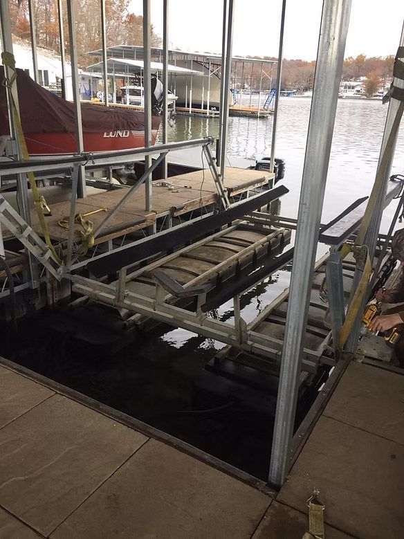 Boat lift at a marina. Lift frame is lowered into water, supports are angled. Other boats, dock visible.